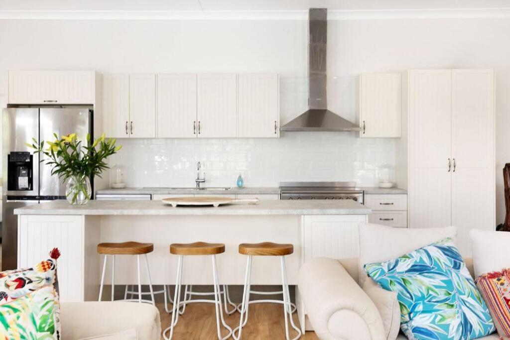a kitchen with white cabinets and a counter with stools at Arborea Country Holiday House catering for 14 to 16 guests In the heart of Bowral in Bowral