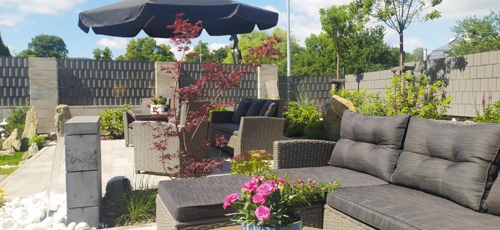 a patio with a couch and an umbrella and some flowers at U Podnóża Zamku in Szczytna