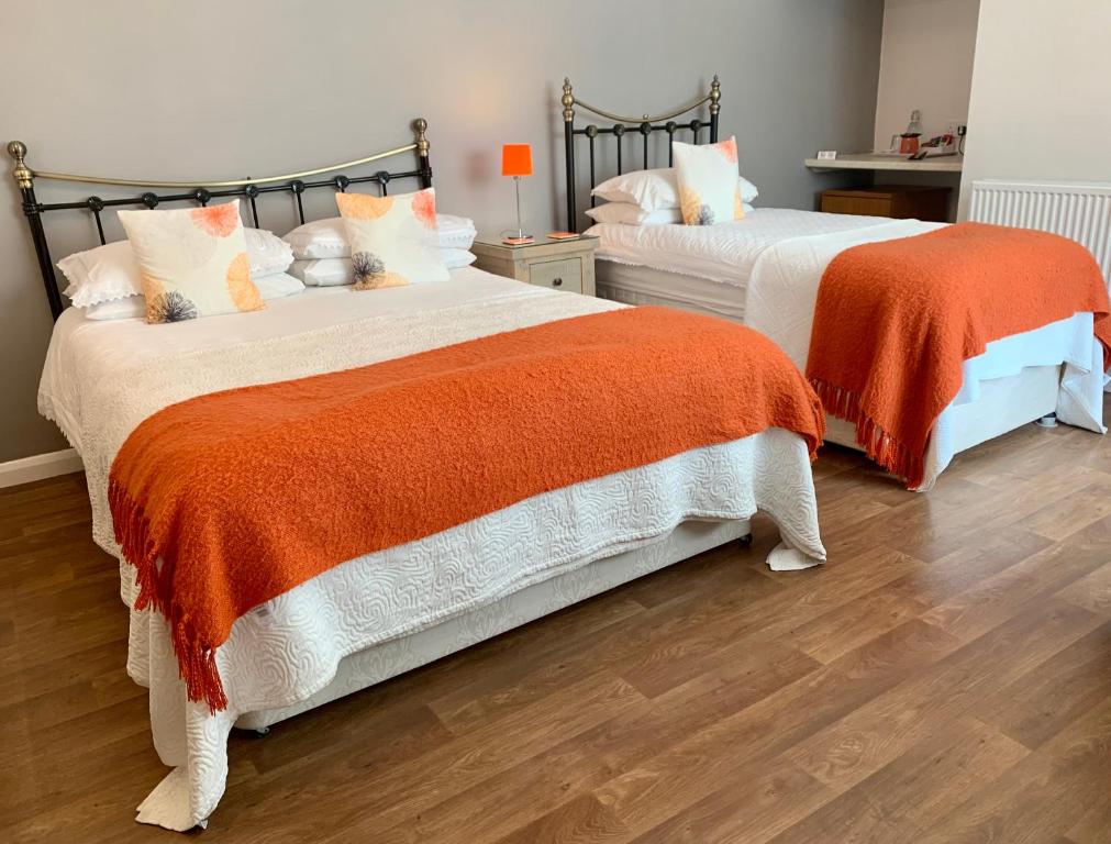 two beds with orange and white sheets in a bedroom at The Coast Yard B & B and Garden Chalets in Selsey