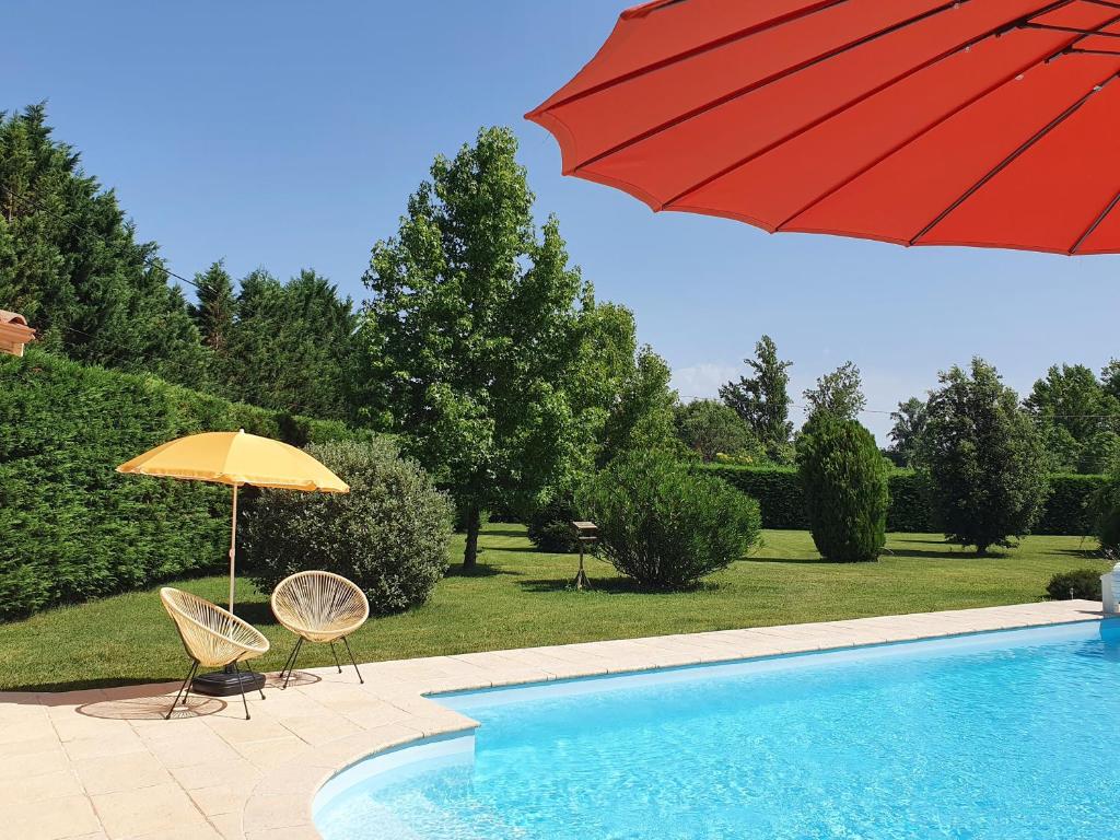 ein roter Regenschirm und zwei Stühle neben einem Pool in der Unterkunft Suite spacieuse avec entrée privative in Lédat