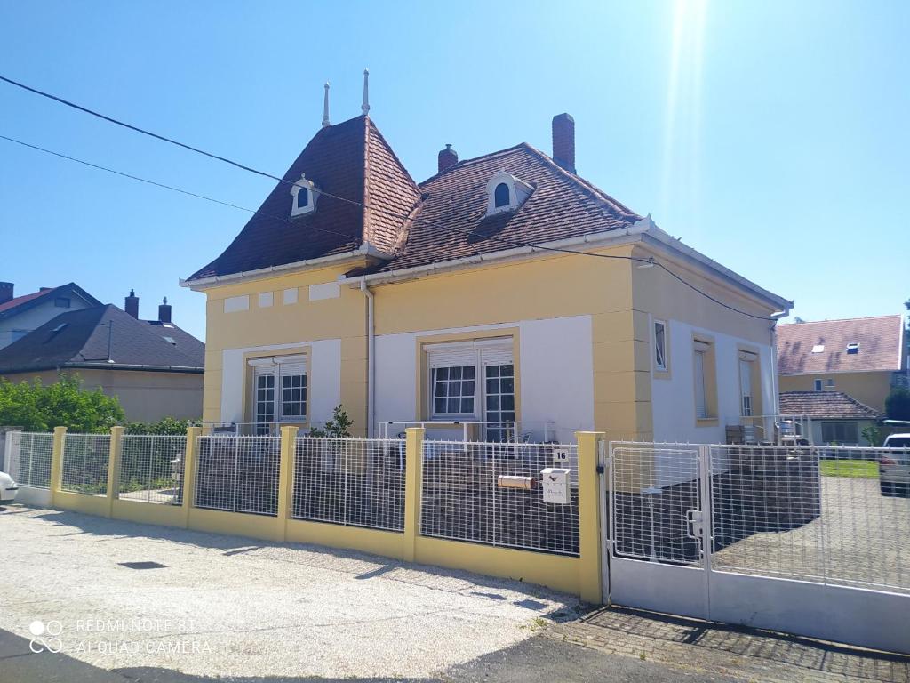 a yellow and white house behind a fence at Villa Vanília in Keszthely
