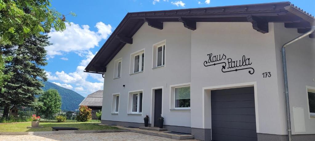 une maison blanche avec un garage et des montagnes en arrière-plan dans l'établissement Haus Paula, à Mallnitz