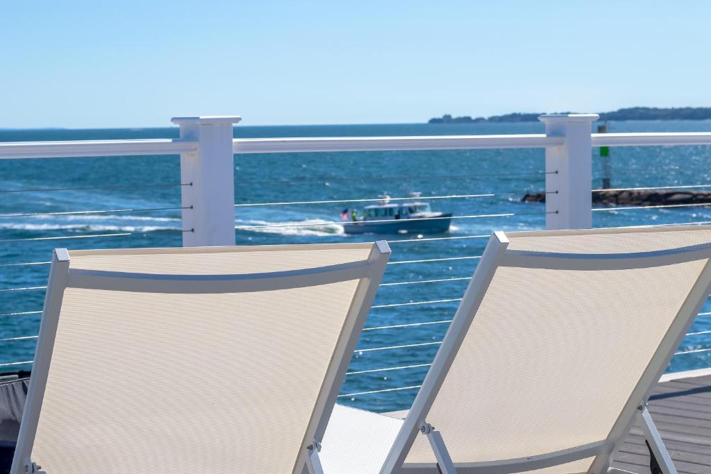 two chairs on a balcony with a boat in the water at Falmouth Tides in Falmouth