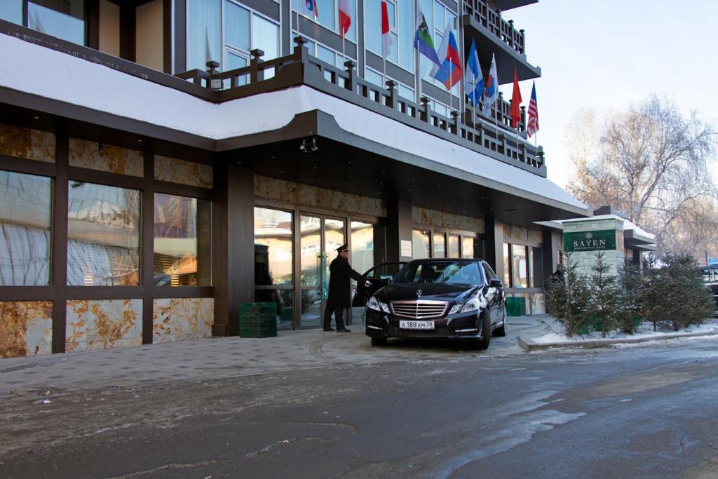 a man standing outside of a building with a car parked outside at International Hotel Sayen in Irkutsk