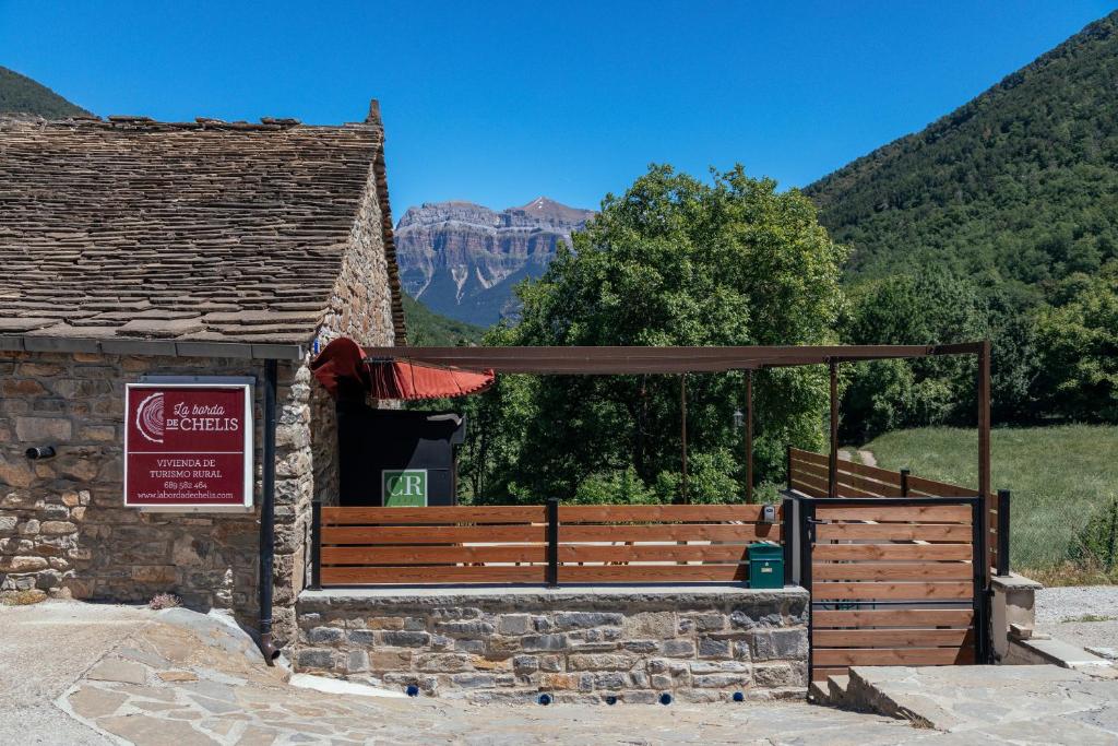 un pequeño edificio con un cartel y montañas al fondo en La Borda de Chelis en Broto