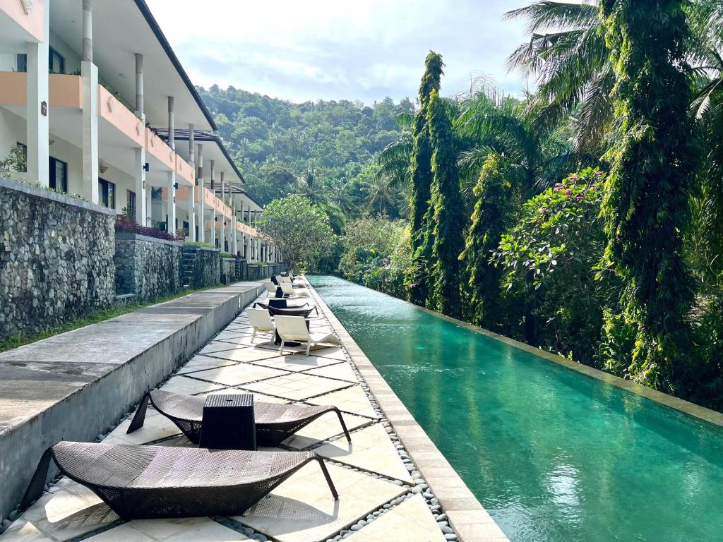 a swimming pool with lounge chairs next to a river at Kebun Villas & Resort in Senggigi