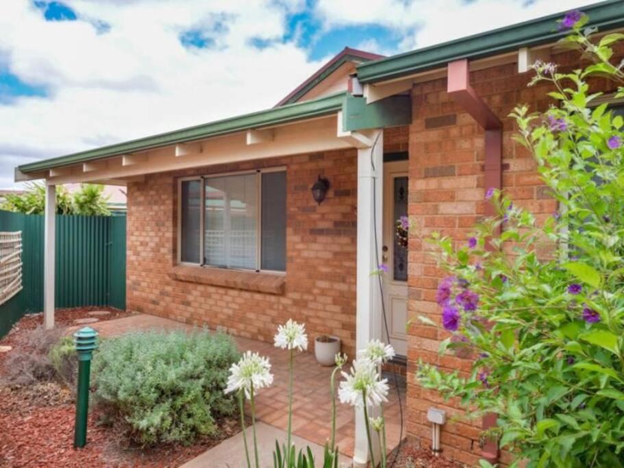 a brick house with a front yard with flowers at Adorable-secure 3 bedroom holiday home with Pool around the corner from The Miners Rest. in Kalgoorlie