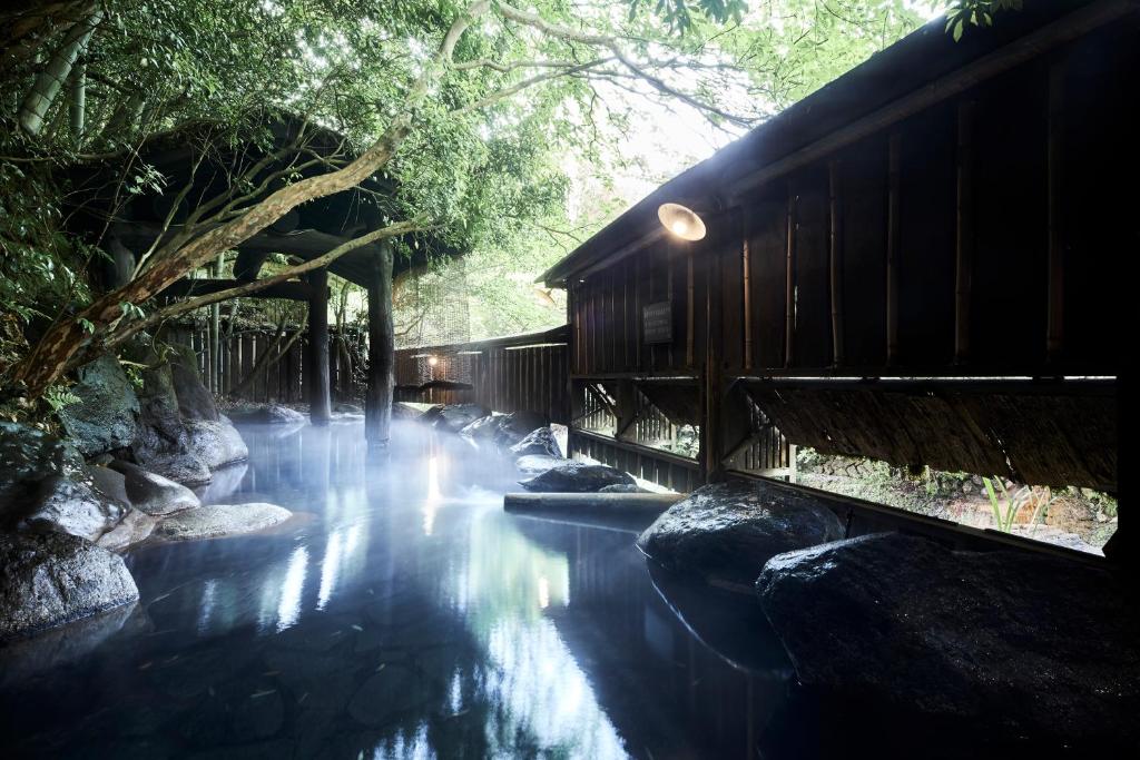 a river with rocks and a building with a waterfall at Fumoto Ryokan in Minamioguni