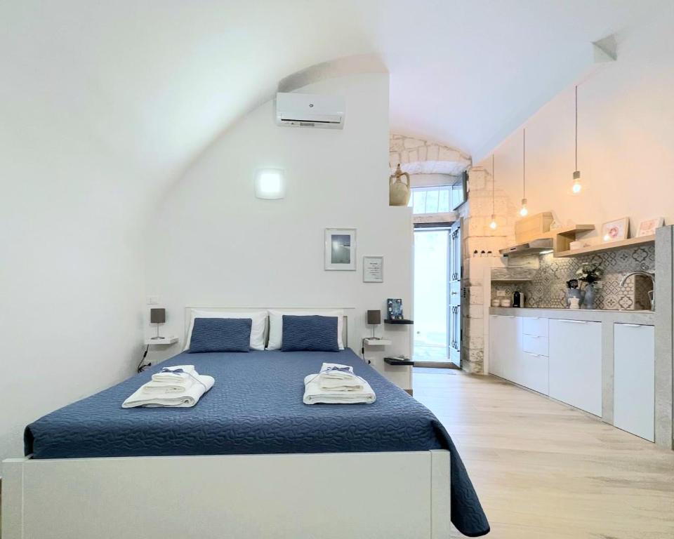 een witte slaapkamer met een blauw bed en een keuken bij La Chicca in Ostuni