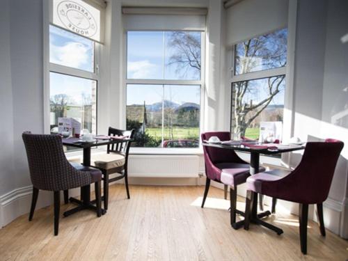 een eetkamer met een tafel, stoelen en ramen bij LakeSide House in Keswick