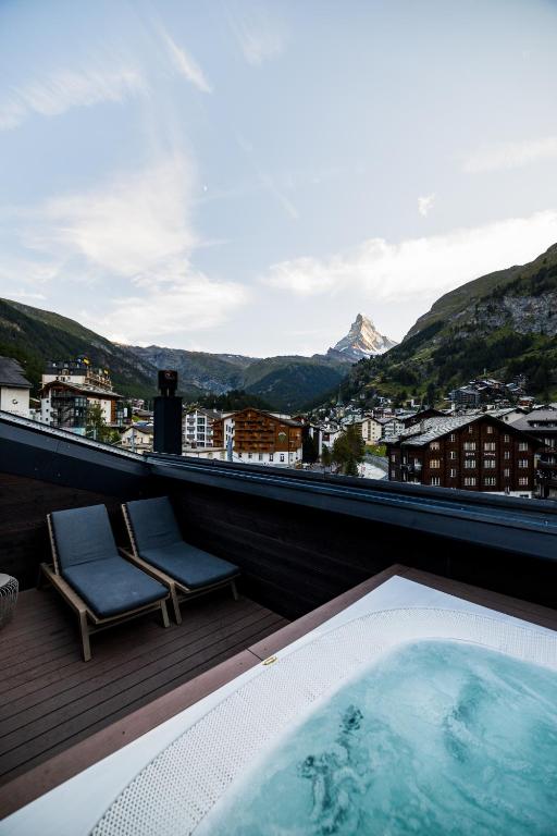 a hot tub on a balcony with a view of the mountains at Hotel ZERMAMA Zermatt in Zermatt