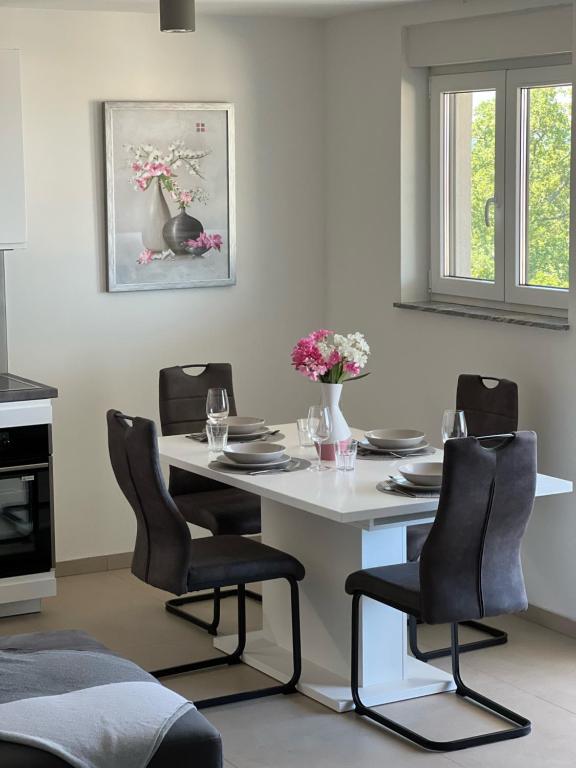 une table blanche avec des chaises noires et une table avec des fleurs. dans l'établissement Apartman Ana, à Sveti Anton