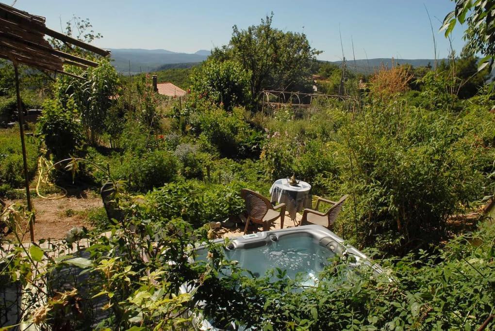 a garden with a hot tub and chairs in the bushes at Cabane et potager sud Cévennes, jacuzzi en option in Roquedur