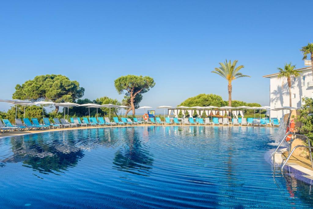 a large swimming pool with blue chairs and palm trees at Garden Playanatural - Adults Only in El Rompido