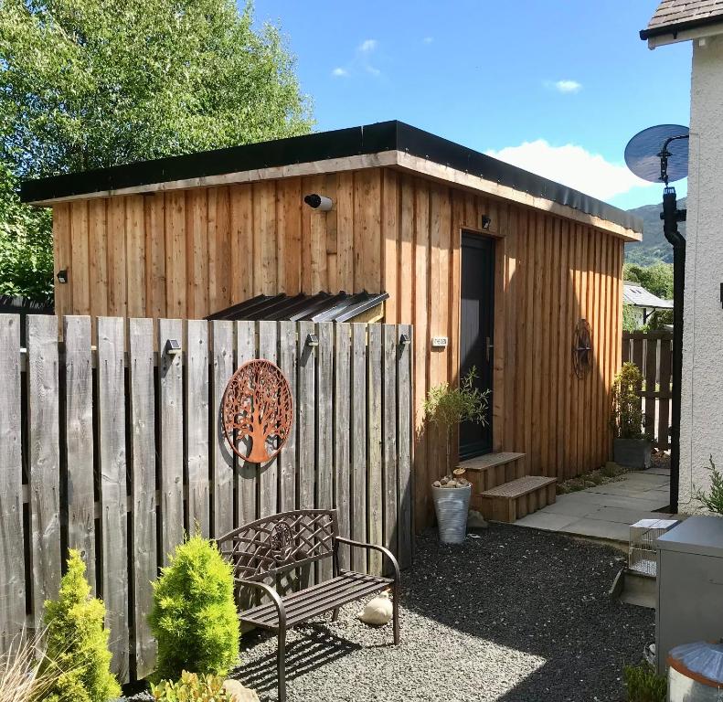 a wooden shed with a bench next to a fence at The Den - your cosy sleepover space in Saint Fillans