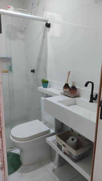 um banheiro branco com vaso sanitário e chuveiro em Apartamento Guarujá Enseada no Guarujá