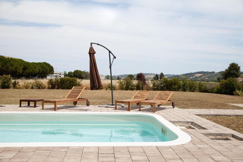 a swimming pool with two benches and an umbrella at Villa Umberto in San Giovanni in Marignano