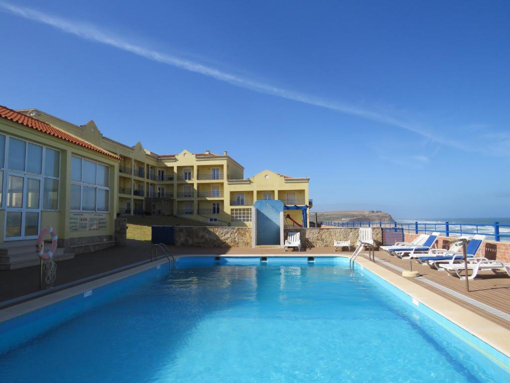 a large swimming pool next to a building and the ocean at Hotel Apartamento Praia Azul in Silveira