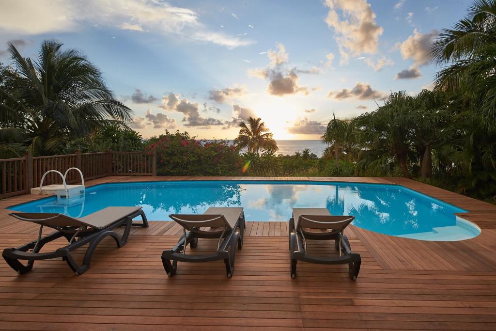 a swimming pool with tables and chairs on a wooden deck at Villa Diodon in Deshaies