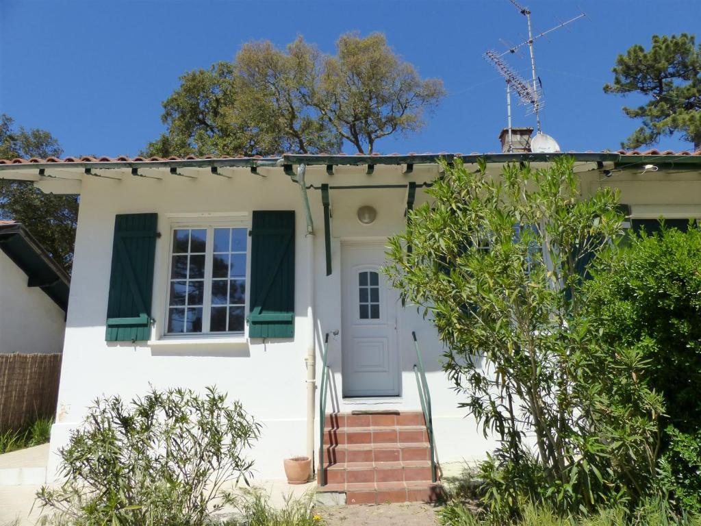 une maison blanche avec des volets verts et une porte dans l'établissement Villa Mitoyenne Pour 4 Personnes Proche Centre-Ville D hossegor, à Hossegor