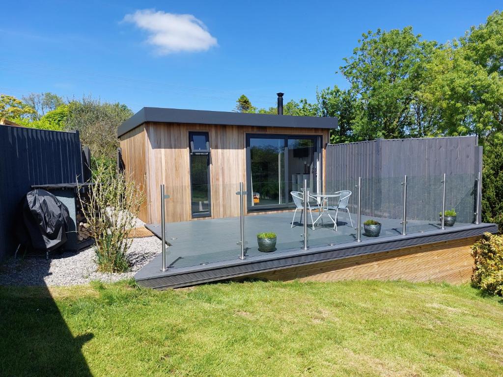 a small cabin with a deck in a yard at The Den - Modern cabin with wood burning stove in Ludchurch