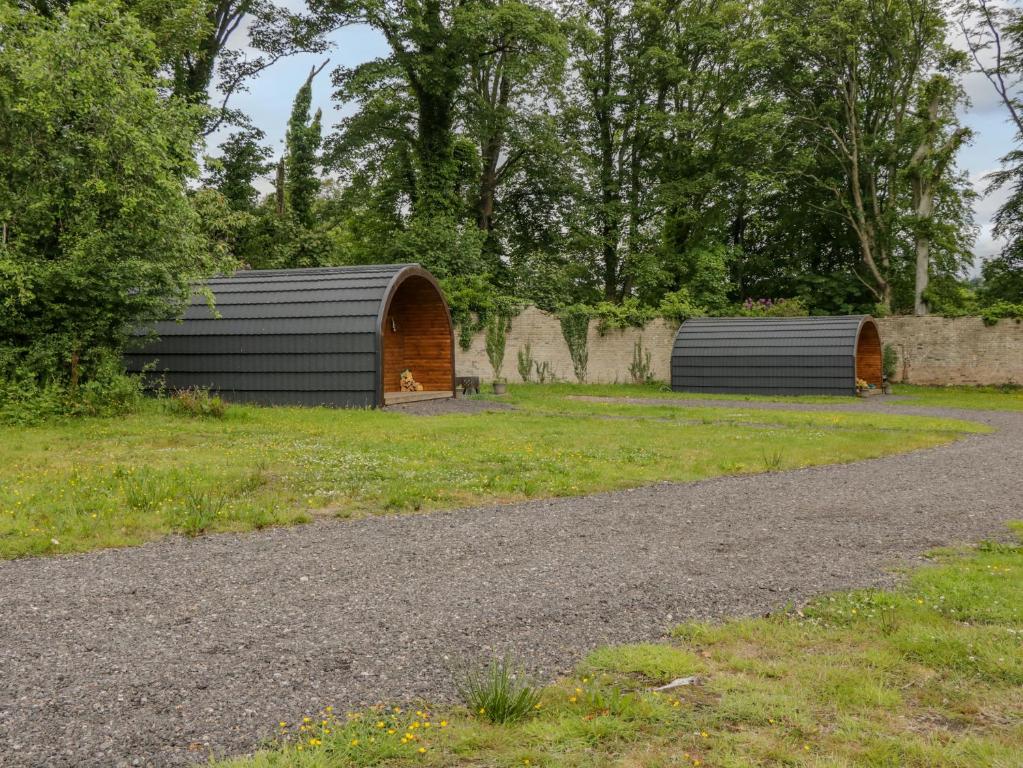 two buildings in a field next to a gravel road at Pod 1 in Seascale