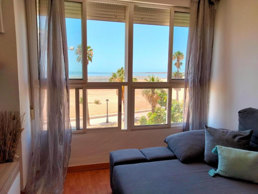 sala de estar con sofá azul y ventana grande en Apto. Trafalgar, playa de la Cachucha. WiFi, A/C, en Puerto Real