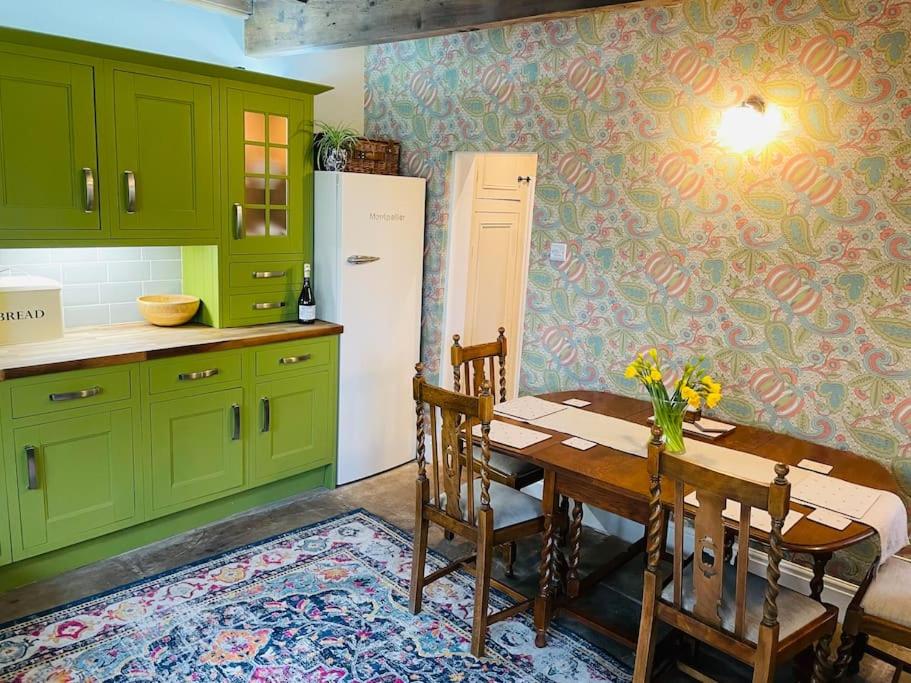 La cuisine est équipée d'armoires vertes, d'une table et d'un réfrigérateur. dans l'établissement Tipple Cottage, à Haworth