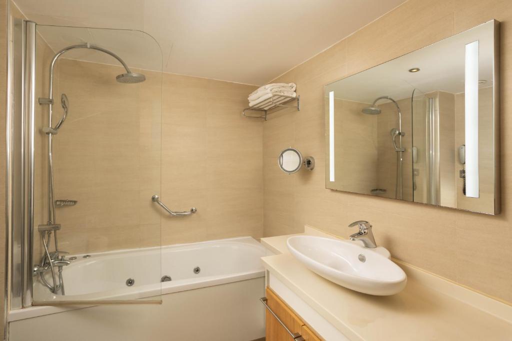 a bathroom with a sink and a tub and a mirror at Atlantica Bay - Adults Only in Limassol