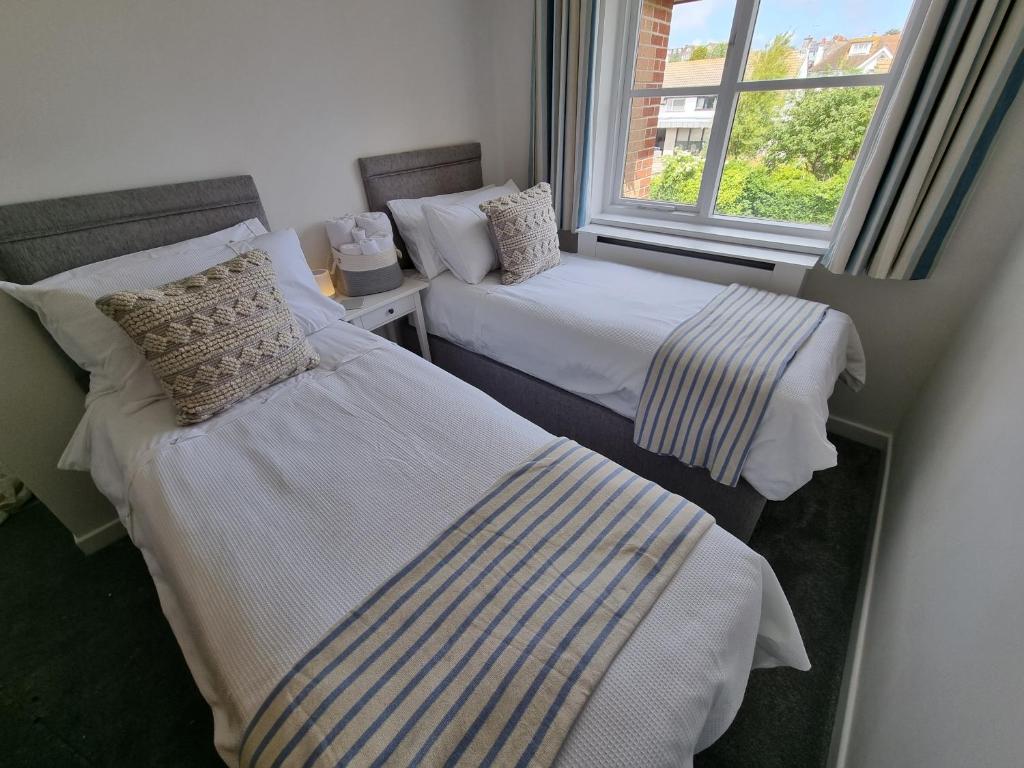 two beds in a room with a window at HighTide - 2 bed with parking, balcony & sea view. in Swanage