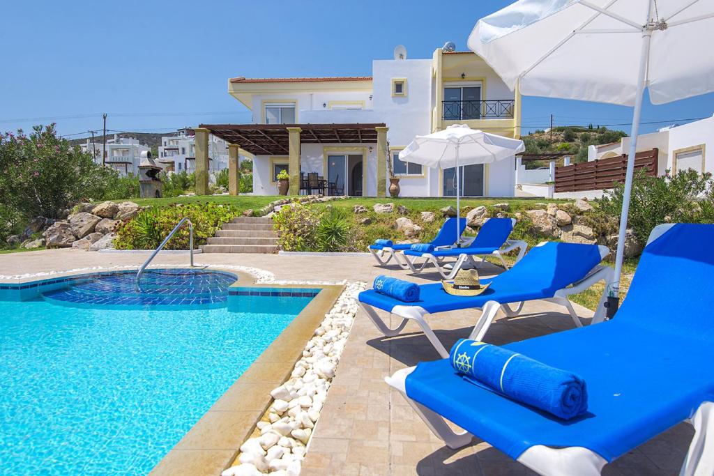 una piscina con sillas azules y sombrillas junto a una casa en Villa Alexi, en Kalathos