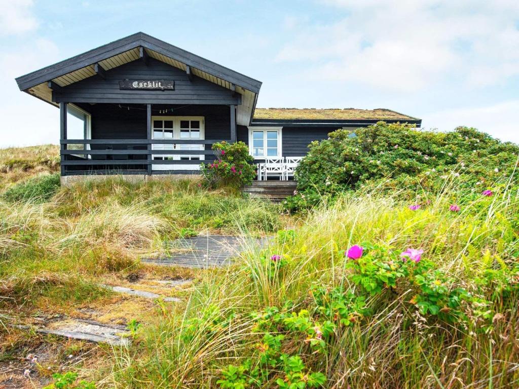 a small black house on a hill with flowers at 6 person holiday home in Ringk bing in Søndervig