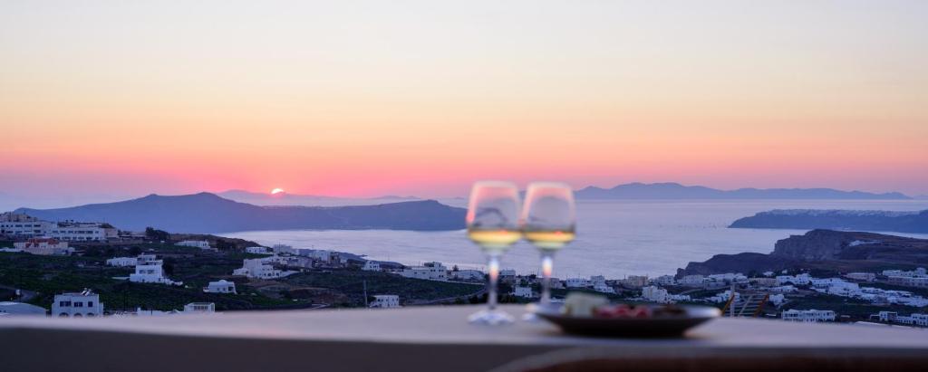 two wine glasses sitting on a ledge with the sunset at Diva Santorini Luxury Villa in Pyrgos