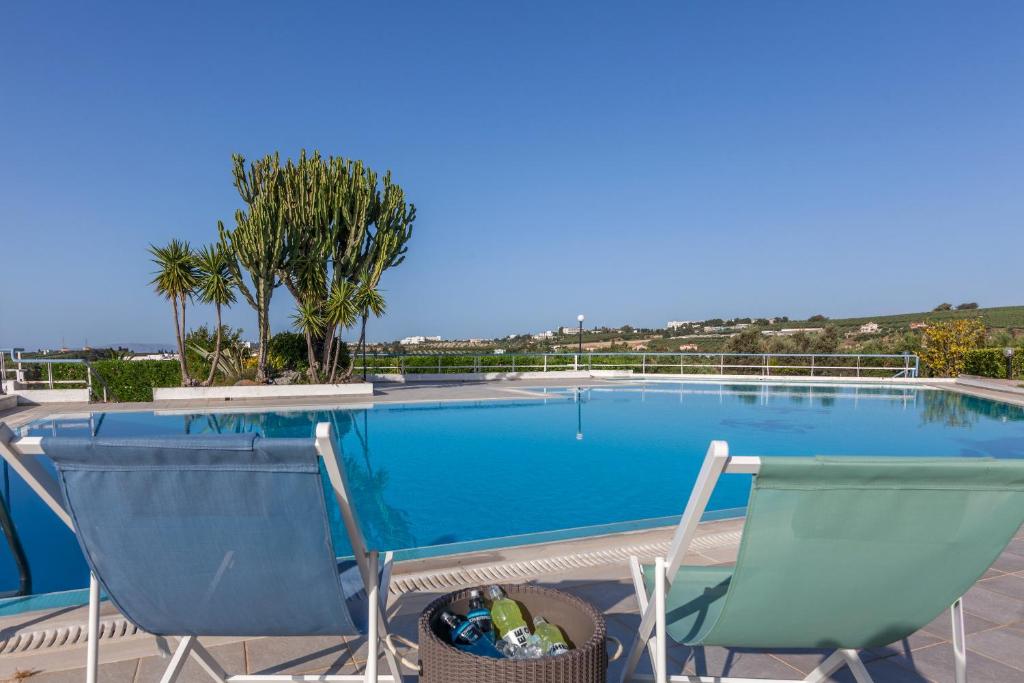 a swimming pool with two chairs and palm trees at Serenity Villa with pool, Kalesa Heraklion in Yiofirákia