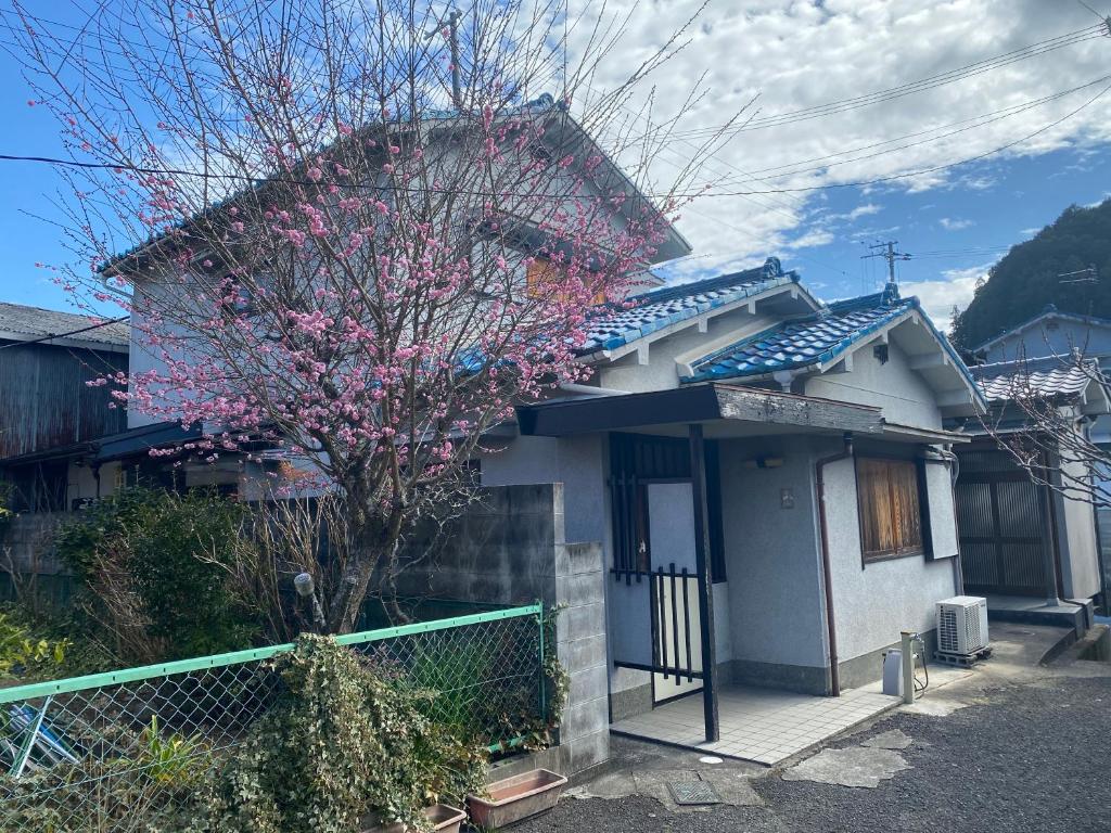 une maison avec un arbre à fleurs devant elle dans l'établissement ゲストハウス　鍼灸院　boshcetto, à Yoshino