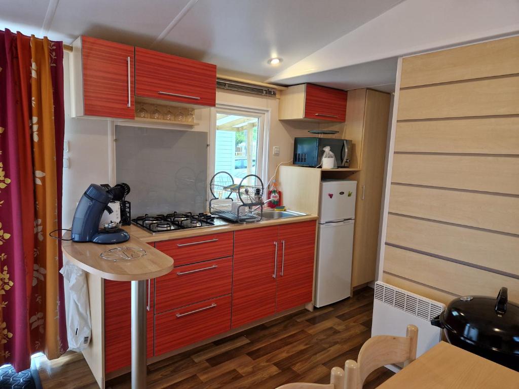 a small kitchen with red cabinets and a white refrigerator at Camping le ried in Boofzheim