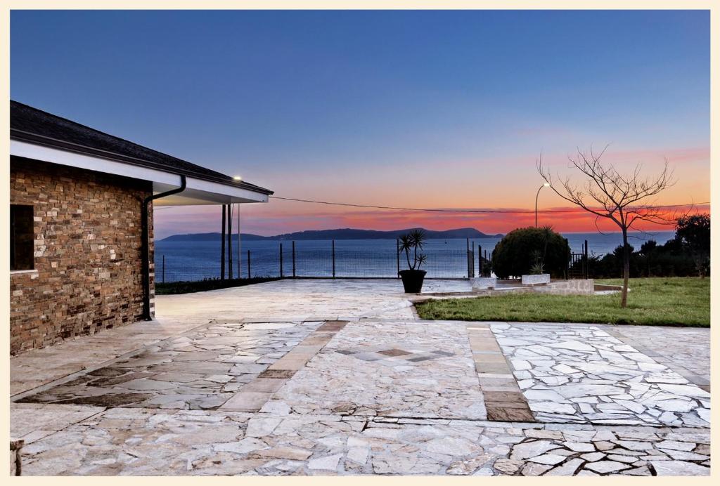 un patio de piedra con vistas al océano al atardecer en VILLA PRAGUEIRA Sanxenxo, en Pontevedra