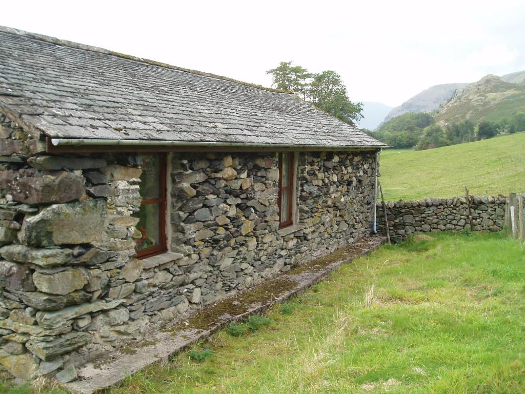 un antiguo edificio de piedra en un campo con una pared de piedra en Fisher-gill Camping Barn, en Thirlmere