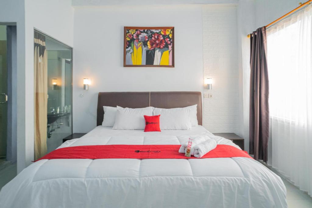 a bed with a stuffed animal laying on a red blanket at RedDoorz @ Kampung Sawah Jatimurni Bekasi in Kampungsawah Dua