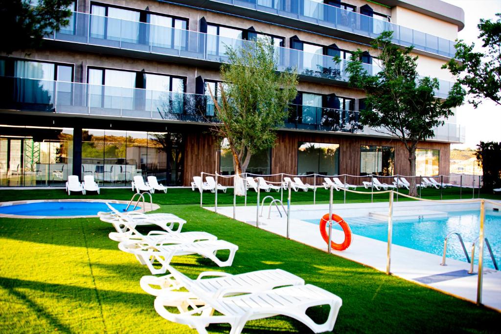 a building with a pool with white lawn chairs and a swimming pool at Hotel Spa Mirador in Jorquera