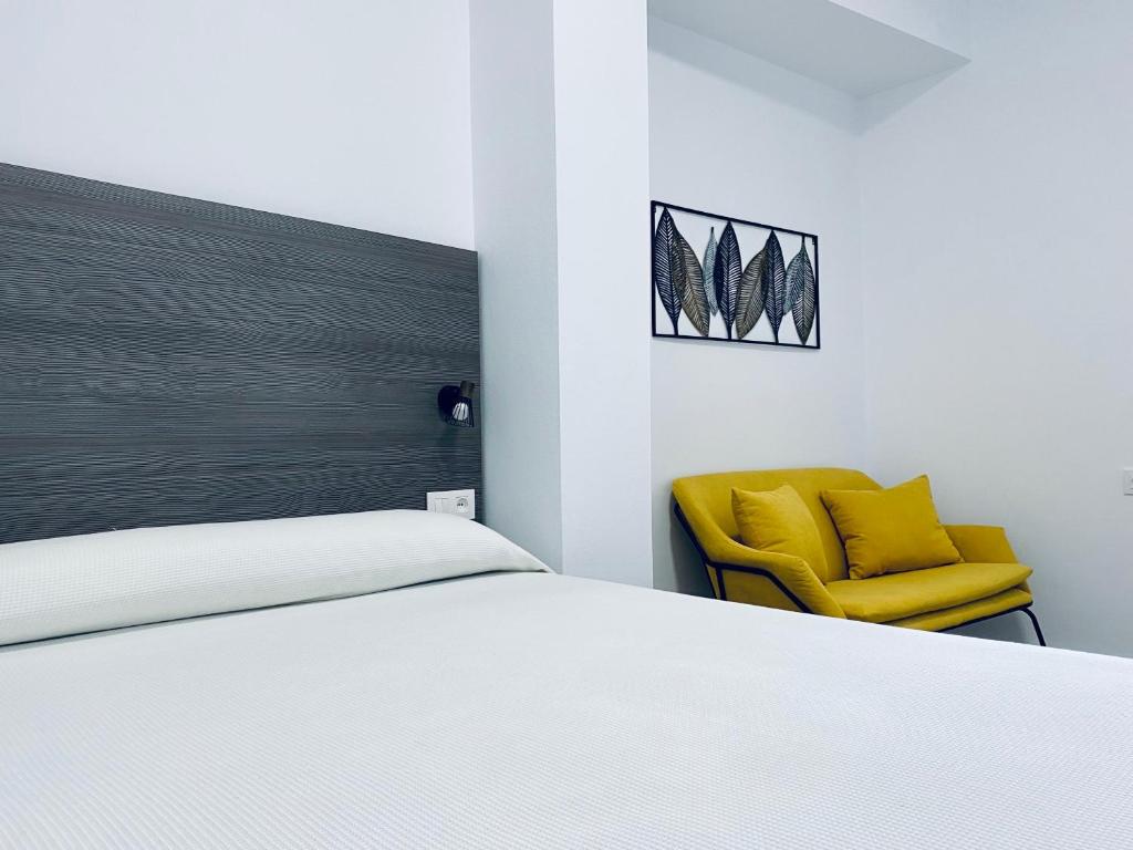 a bedroom with a bed and a yellow chair at Apartamentos Turísticos Santo Rostro in Chipiona