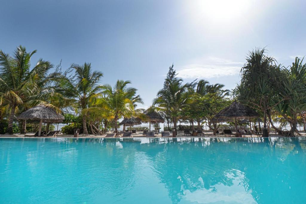 a beach with a pool and palm trees at Mwezi Boutique Resort in Jambiani