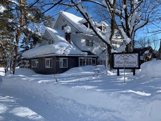 a snow covered house with a sign in front of it at Lodge Blue Mount Hakuba in Hakuba