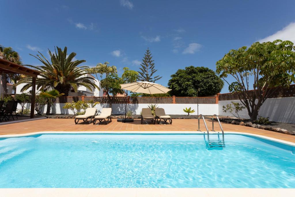 a swimming pool in a yard with chairs and an umbrella at Villa Casiopea in Corralejo