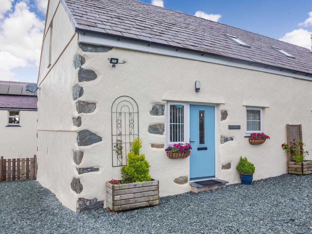 a white cottage with a blue door and flowers at Marchlyn in Caernarfon