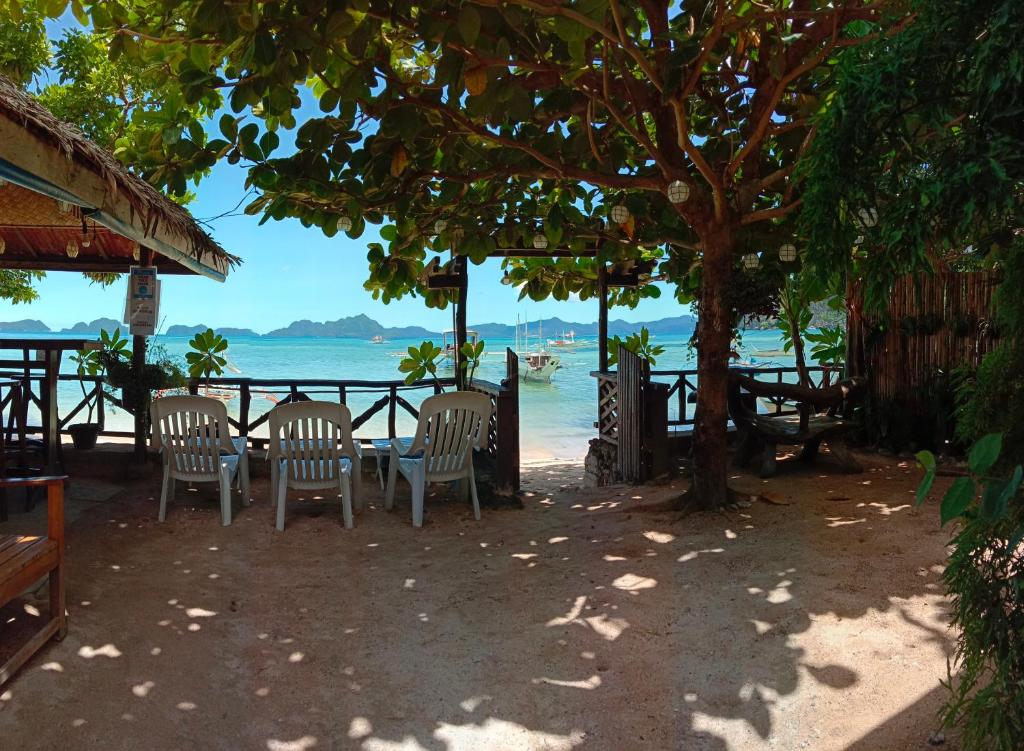 una mesa y sillas bajo un árbol en la playa en Corong Beach Resort, en El Nido