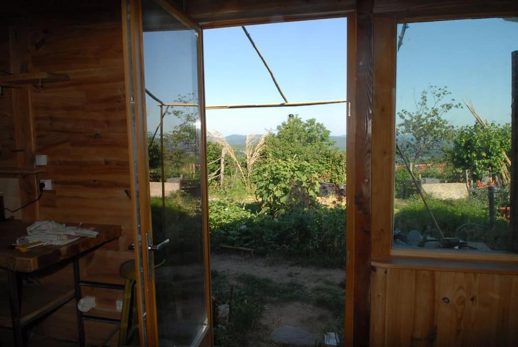 an open glass door with a view of a yard at Cabane et potager sud Cévennes, jacuzzi en option in Roquedur