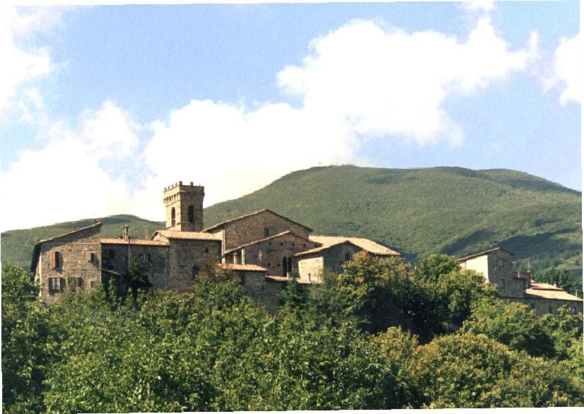 un antiguo edificio en una colina con montañas en el fondo en AFFITTACAMERE SANT'ANGELO en Abbadia San Salvatore