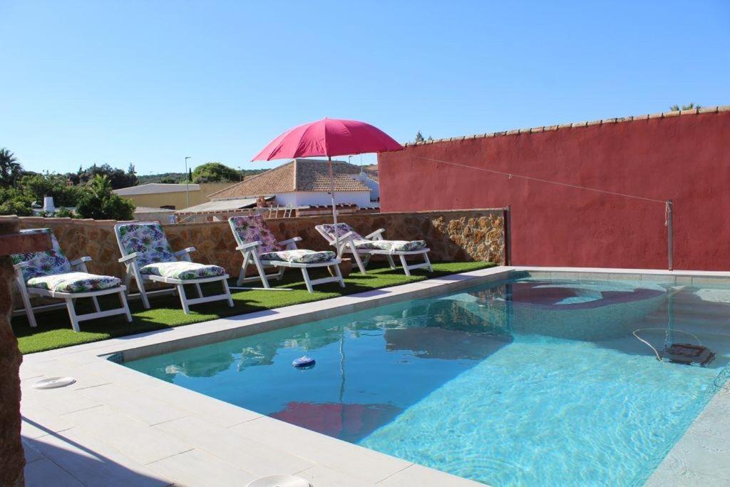 een zwembad met een rode parasol en stoelen en een tafel bij Casa Rural LA ENCINA in Hornachuelos