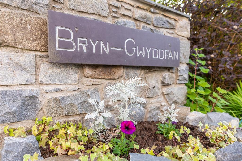 a sign on the side of a stone wall with flowers at Llanberis Lodges in Llanberis